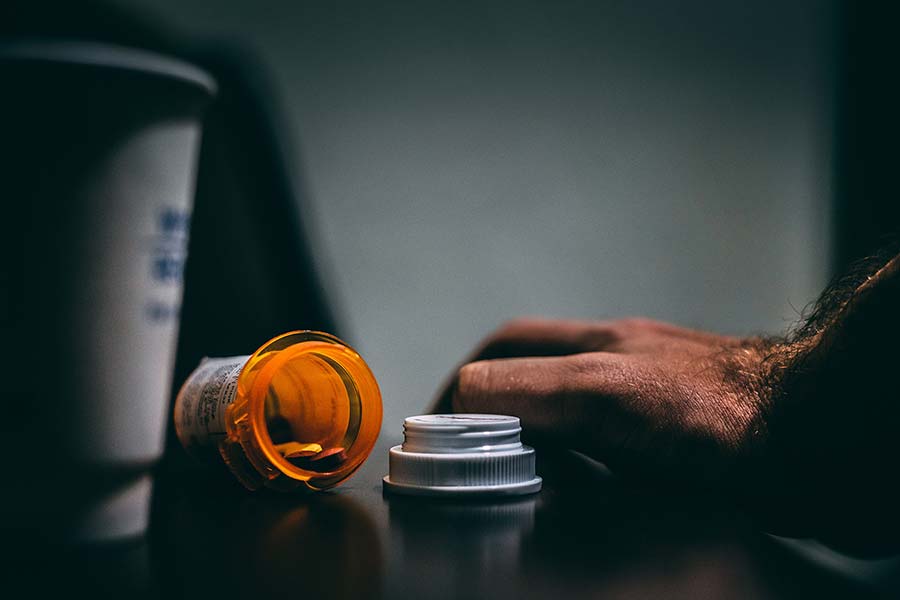 Open prescription pill bottle laying on its side next to a man's hand.