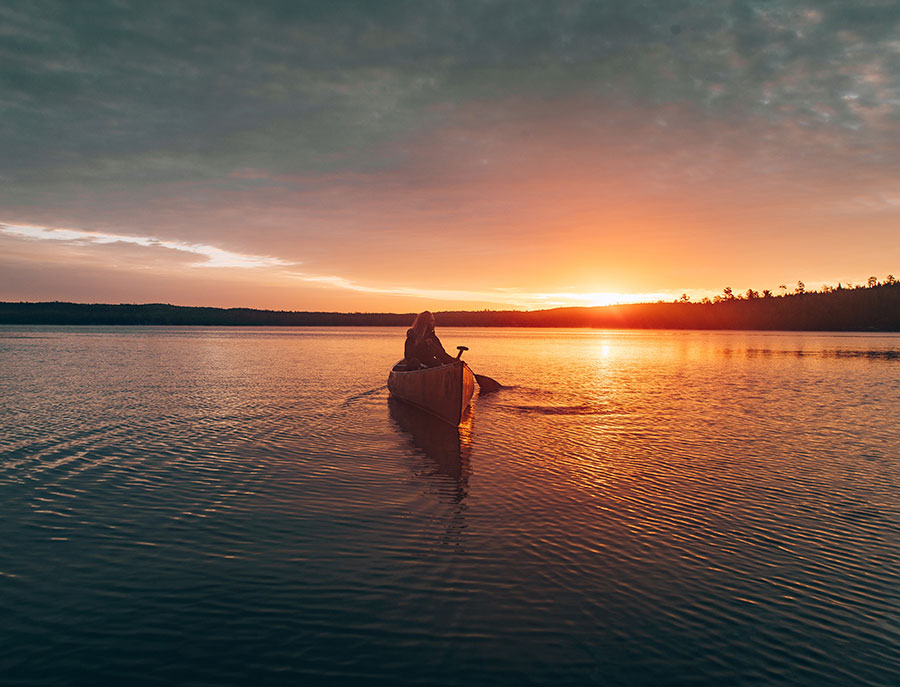 Woman in canoe on a vast lake in front of a sunset.